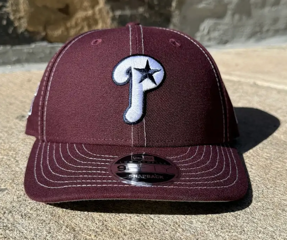 Maroon baseball cap with a logo on a stone surface