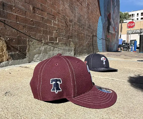 Two baseball caps on a concrete surface with a brick wall and graffiti in the background.