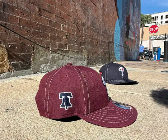 Two baseball caps on a concrete surface with a brick wall and graffiti in the background.