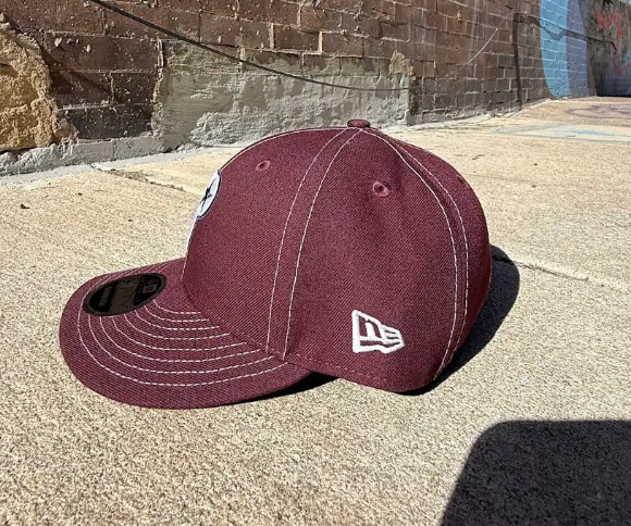 Maroon baseball cap with New Era logo on a concrete surface