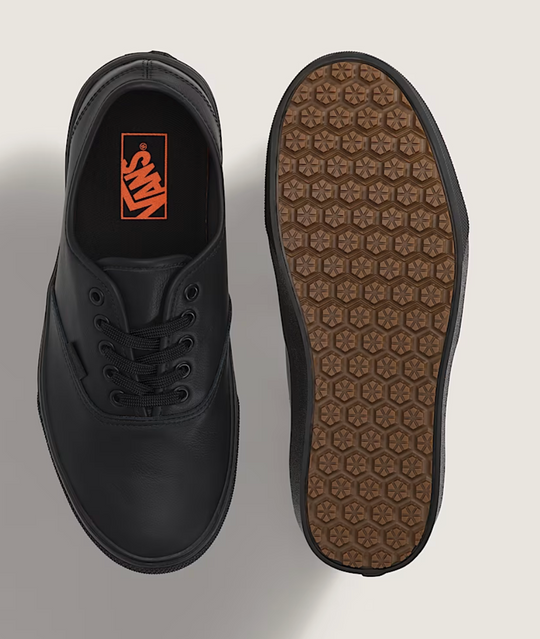 Black shoe with orange logo on the side and brown sole on a light gray background
