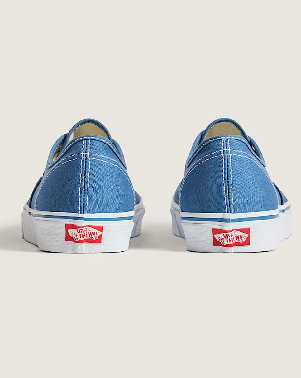 A pair of blue canvas low-top sneakers shown from the back, featuring white rubber soles with a red Vans logo.