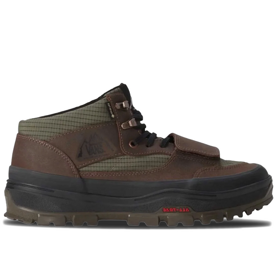 A Vans mid-top outdoor boot in brown and olive green, featuring a lace-up front, a hook-and-loop strap closure, and a rugged black and brown sole, shown against a plain white background.