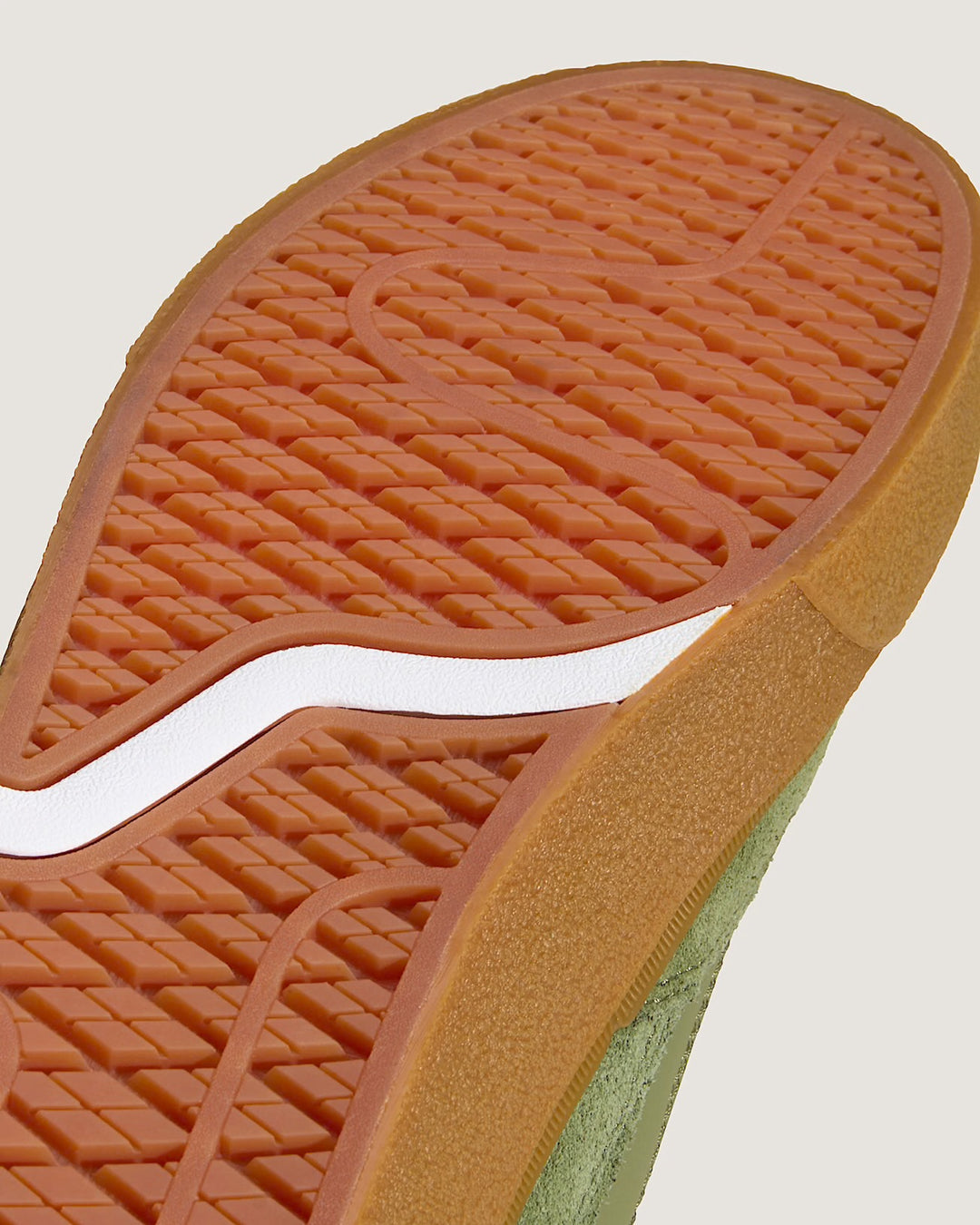 Close-up of a shoe sole with brown rubber outsole and green inner sole on a light gray background