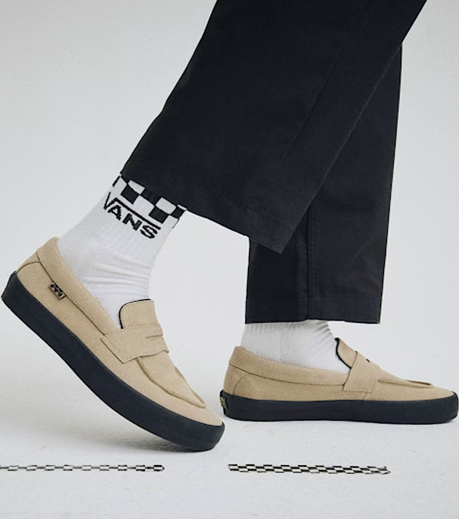 Beige loafers with black soles worn with white socks and black pants