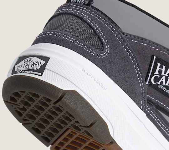 Close-up of a gray Vans shoe with brand logos on a light gray background