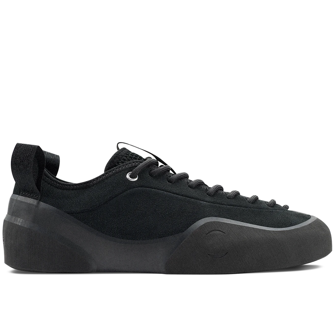 A black low-top sneaker with a chunky platform sole, black laces, and a pull tab on the heel, shown from a side profile against a white background.