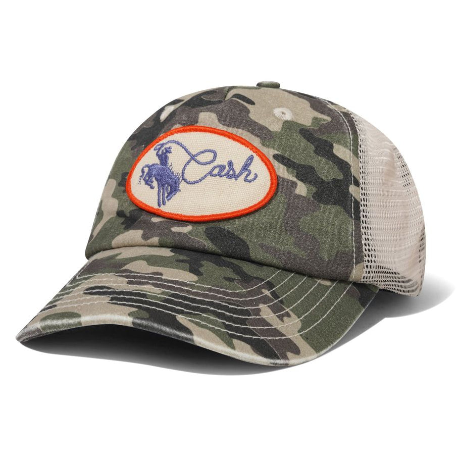 A camouflage trucker cap with a beige mesh back and a circular embroidered patch on the front featuring the brand name 'Cash' in blue with a horse logo inside an orange border.