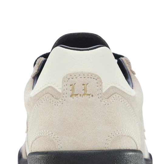 Close-up of a beige sneaker with a logo on the side against a light gray background